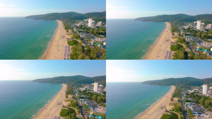 空中4k视图飞越热带蓝色海洋，朝向美丽的绿色山脉和白色沙滩。泰国。普吉岛。卡伦海滩。棕榈滩。岛屿俯视