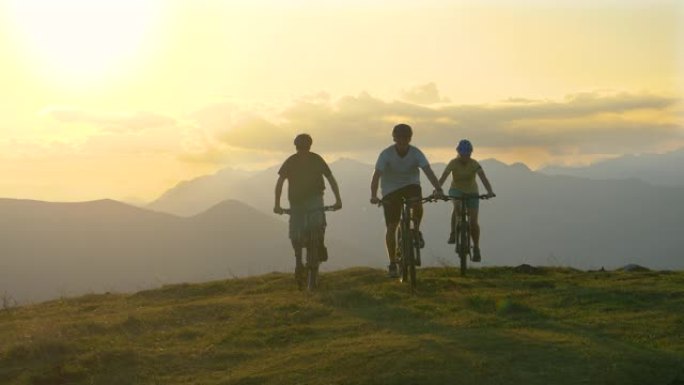 在一个阳光明媚的夜晚，三名运动游客骑着电动自行车穿过草地。