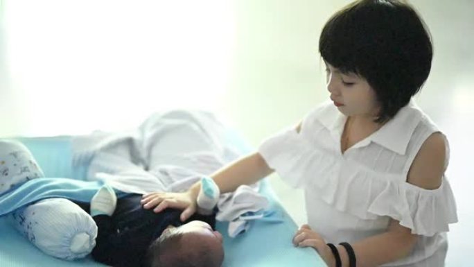 一个亚洲中国小女孩照顾她的小弟弟，把他放在卧室里睡觉