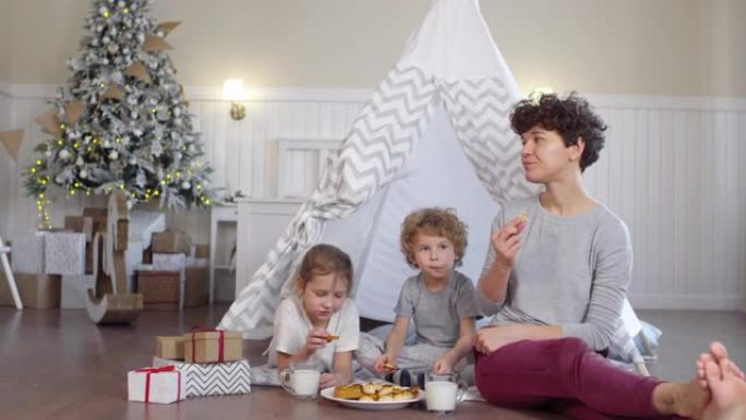 快乐的母亲和孩子们在房间里用圆锥形帐篷和圣诞树吃饼干