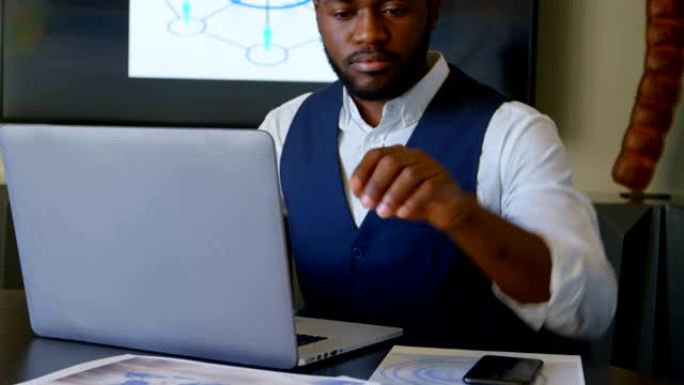 年轻黑人商人在现代办公室4k中使用笔记本电脑时看文件的前视图