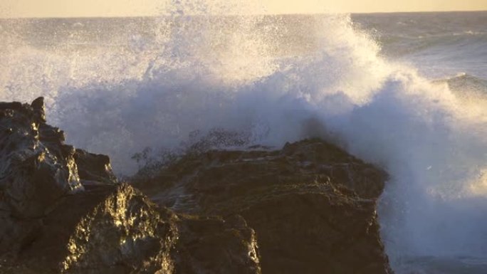 愤怒的泡沫海浪在日落光线中慢慢压在岩石海岸上。慢动作视图