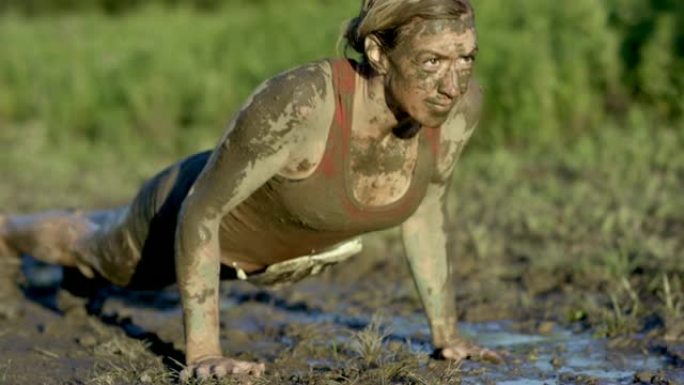 成年女性在有趣的跑步中在泥泞中俯卧撑