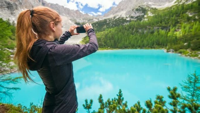 在晴朗的日子里，一名女性徒步旅行者在多洛米特的Sorapiss山湖用智能手机拍照