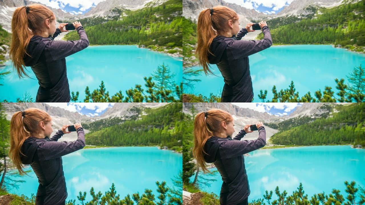 在晴朗的日子里，一名女性徒步旅行者在多洛米特的Sorapiss山湖用智能手机拍照