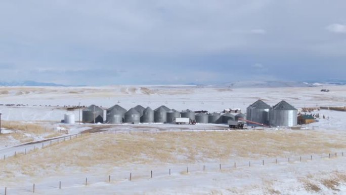 空中: 在蒙大拿州白雪皑皑的平原上绕着大型金属存储筒仓飞行。