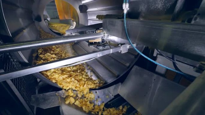 工厂设备在机器中旋转薯片，添加增味剂。