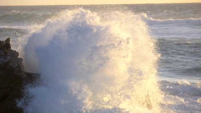 海浪在日落光线中猛烈地冲向岩石。水花在夕阳的灯光下慢慢落到地上。慢动作镜头