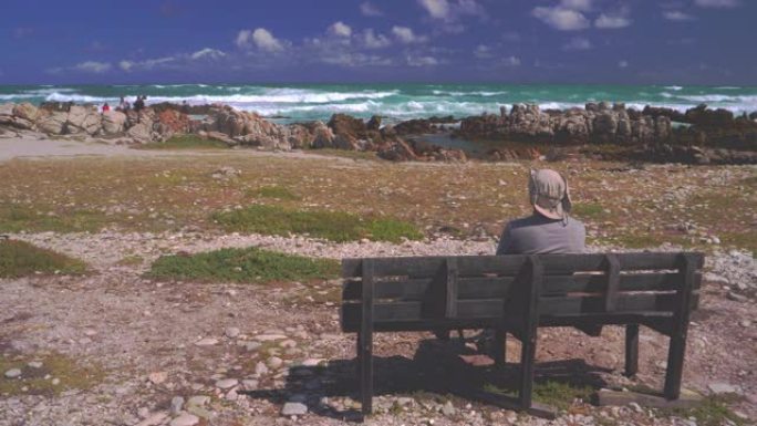 男人坐在海边的长椅上，欣赏美景