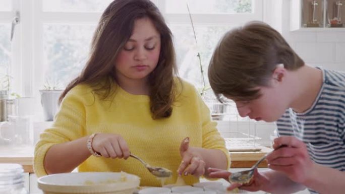年轻的唐斯综合症夫妇将混合物放入家里厨房的纸杯蛋糕盒中