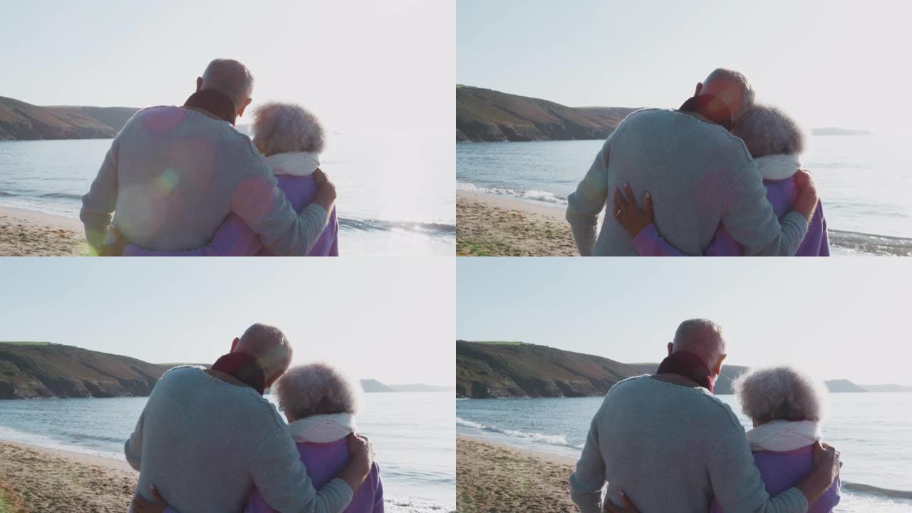 热爱活跃的老年夫妇在寒海滩度假时沿着海岸线散步的后视图