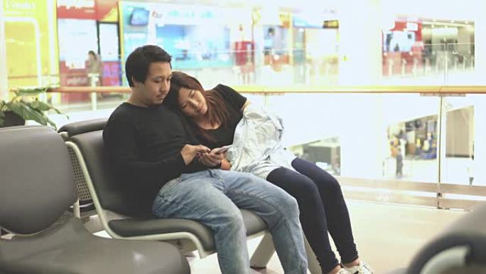 4k镜头亚洲夫妇旅客坐和睡觉的场景，她的行李等待航班呼叫在机场航站楼，运输和旅客旅行的概念