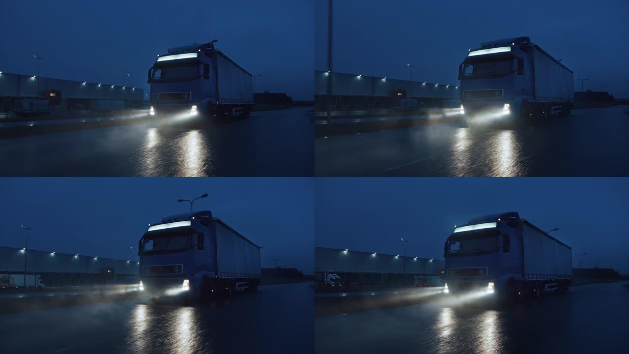 蓝色长途半卡车，满载货物的拖车在夜间在高速公路上行驶，穿过雨、雾、雪穿越大陆。工业仓库区。正面跟随镜