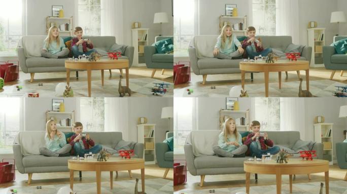 在家: 聪明的男孩在视频游戏机上玩耍，使用操纵杆控制器，他的姐姐坐在沙发旁为他欢呼。快乐的孩子一起玩