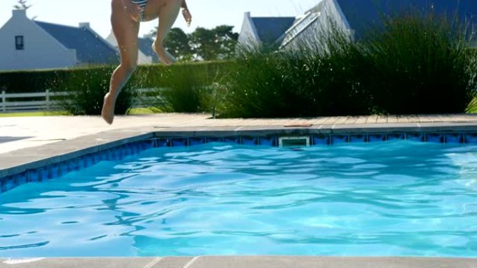 阳光明媚的日子里，年轻的混血女子在游泳池里跳跃的前视图4k