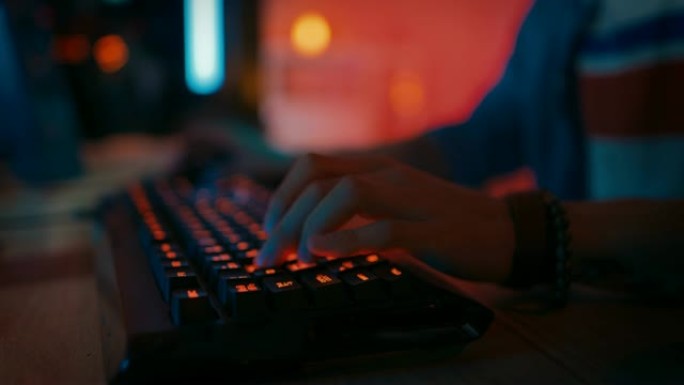特写镜头显示玩家在玩在线视频游戏时按下键盘按钮。键盘发光二极管灯在彩虹光谱中变色。玩家戴着手镯。房间