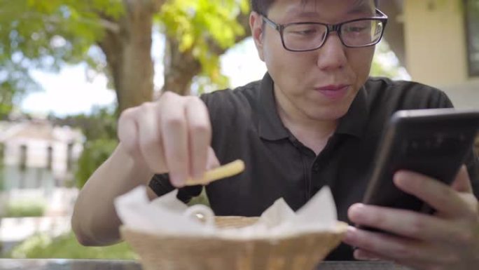 男人在户外吃很多炸薯条并使用智能手机