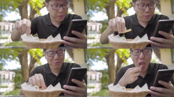 男人在户外吃很多炸薯条并使用智能手机