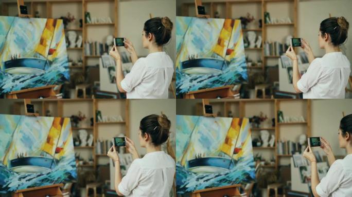 女画家正在独自站在工作室里，使用现代智能手机相机触摸屏拍摄她美丽的照片。现代技术和艺术概念。