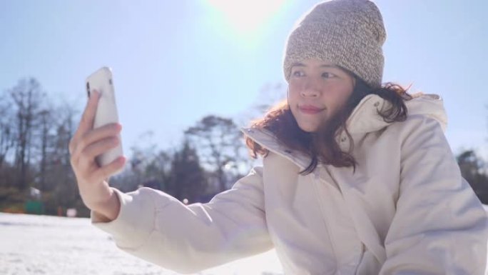 亚洲旅游女子在雪公园拍摄社交媒体自拍照。
