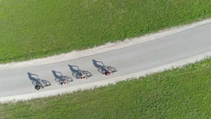 自上而下: 四个朋友骑自行车在空旷的柏油路上投下阴影。