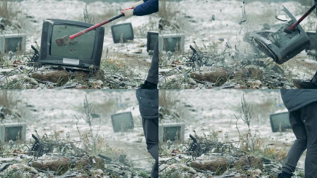 一个人在垃圾填埋场用锤子砸碎旧电视。一名男子撞坏了旧电视机。