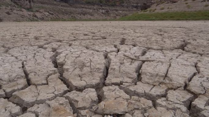 由于气候变化和全球变暖造成的干旱，在干燥大坝的破裂泥浆表面上躺着死鱼的4k特写倾斜视图