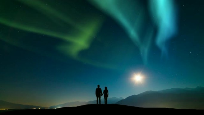 这对夫妇站在山上，面对着北极光的天空。时间流逝
