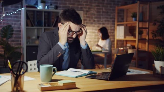 疲倦的上班族使用电脑感到头痛晚上睡在桌子上