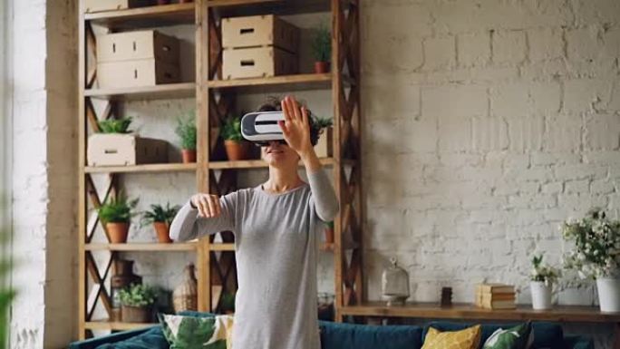 苗条的女孩正在家里使用虚拟现实眼镜，站在阁楼风格的房间里，移动手玩游戏。现代科技、休闲和新体验理念。