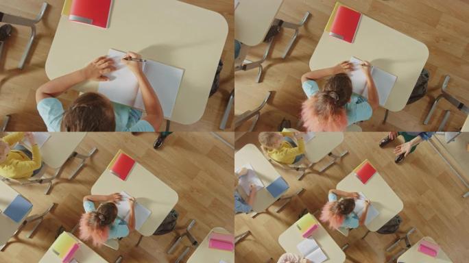 小学教室: 坐在课桌前的女孩在练习笔记本上做作业。从练习册开始缩小俯视图。