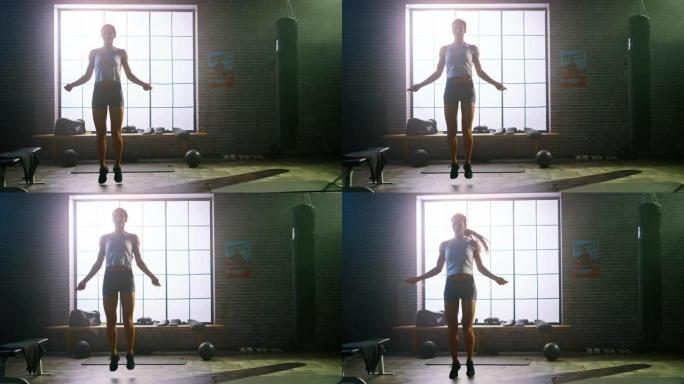 强壮的运动女性在阁楼风格的工业健身房用跳绳锻炼。她专注于激烈的交叉健身训练项目。她身后的大窗户。