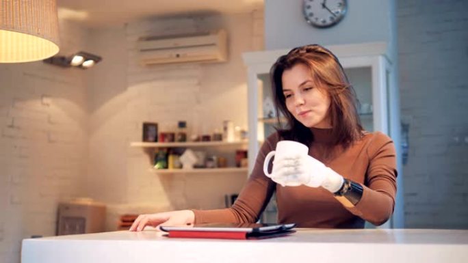 用仿生手微笑的女士正在从杯子里喝水并操作平板电脑