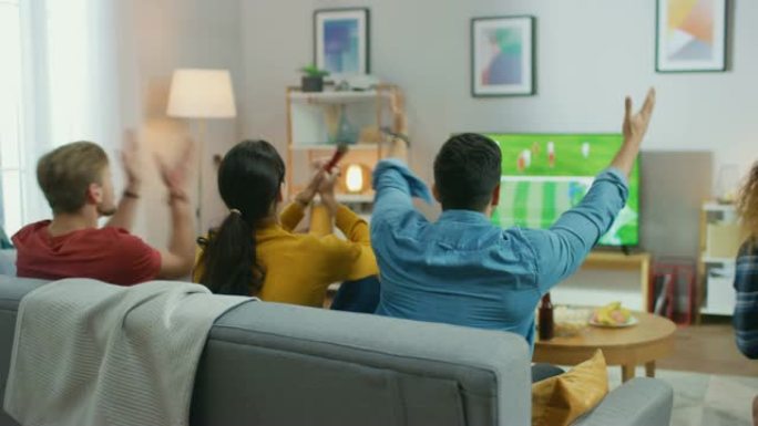 在家里，一群不同的体育迷在电视上观看重要的足球比赛，他们为球队加油，在球队进球后庆祝胜利。舒适的房间