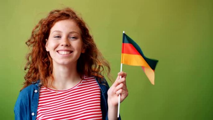 美丽的红发女孩举着德国国旗在绿色背景上微笑