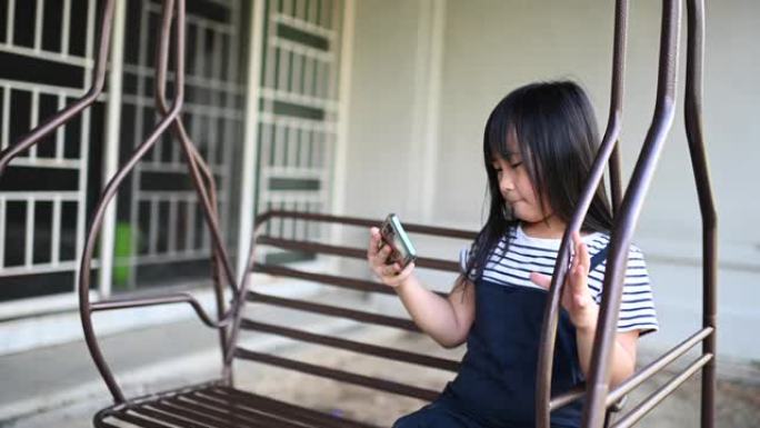 一位亚洲华裔年轻女孩坐在自家后院的秋千上享受下午的时光，同时在手机上玩游戏