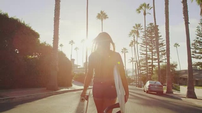 迷人的冲浪女孩在日落时带着滑板走在街上，带着镜头耀斑