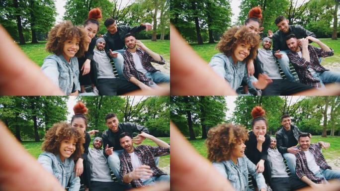 在阳光明媚的日子里，一群不同种族的年轻朋友的慢动作在绿色城市公园里玩得开心，并用手机自拍