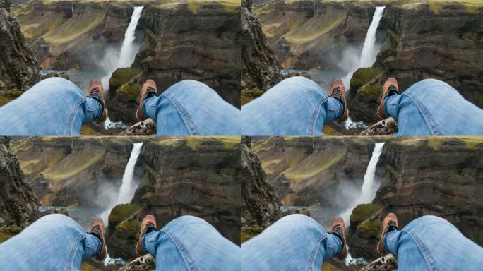 坐在悬崖上的观点，看着峡谷中的瀑布，用脚晃来晃去