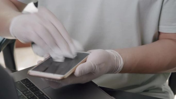 亚洲男子使用消毒湿巾清洁他的智能手机或移动设备的屏幕，以清洁和抗菌冠状病毒或新型冠状病毒肺炎问题在家