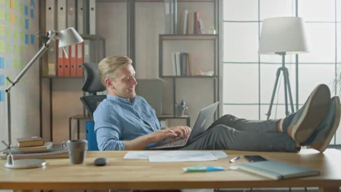 成功的年轻企业家在笔记本电脑上工作，双腿放在桌子上。设计师使用笔记本创建软件独角兽启动。为大学写论文