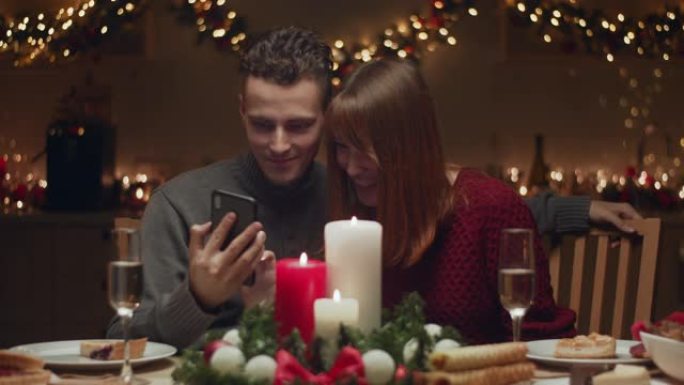 夫妇看起来像智能手机。他们在厨房的房子里庆祝圣诞节。