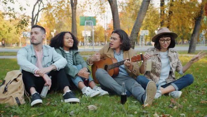 城市公园里快乐的女孩和男孩在草地上唱歌弹吉他的肖像