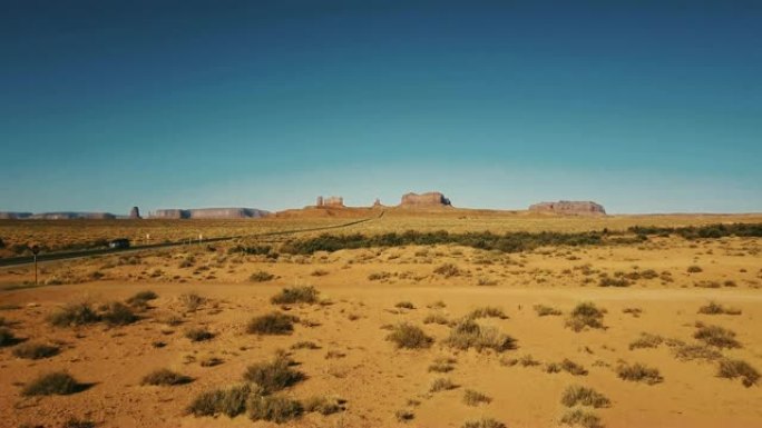 无人机在亚利桑那州和犹他州的纪念碑谷附近的干燥的美国砂岩沙漠上空低空飞行，晴朗的蓝天。