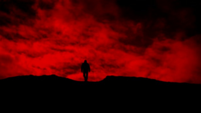 男子在红色的天空轮廓上走过山坡