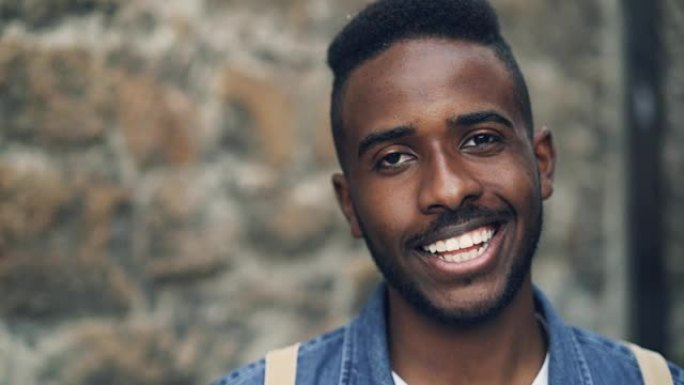 情绪激动的非洲裔美国男子的特写慢动作肖像笔直地看着相机，然后开心地微笑着对好消息做出反应。人和情感概
