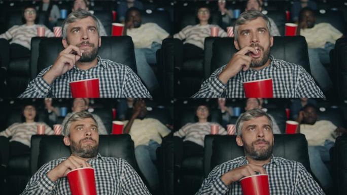 成熟的家伙在黑暗的现代电影院里看恐怖电影吃爆米花