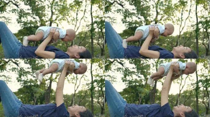 女人在公园里举起可爱的男婴的乐趣。年轻的亚洲母亲带着幸福的情感在公园或花园高高举起她的宝贝儿子。慢动
