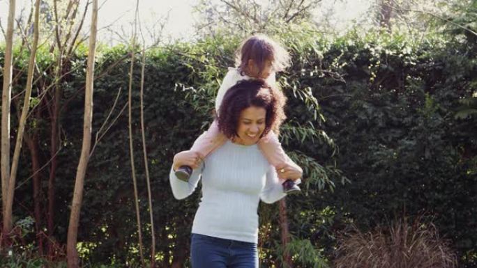 母亲在家里的花园里给年幼的女儿骑在肩膀上