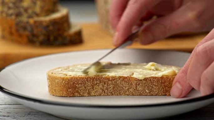 女性用刀将黄油涂在一片面包上。背景中模糊的两种面包。滑块镜头，4K